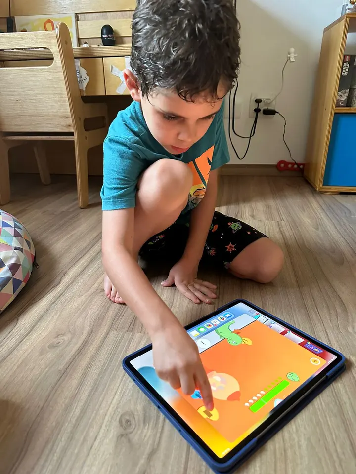 Um menino sentado no chão joga o Domlexia em um tablet, tocando a tela com o dedo